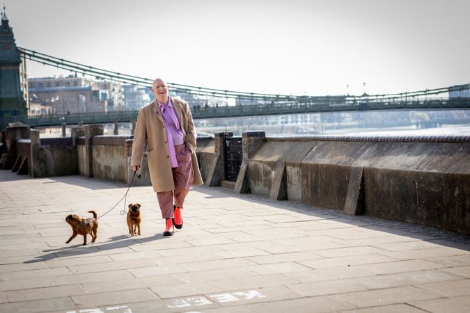 Smiling man walking by river with two small dogs