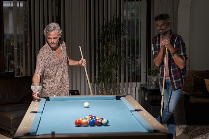 Mature men playing pool game in apartment