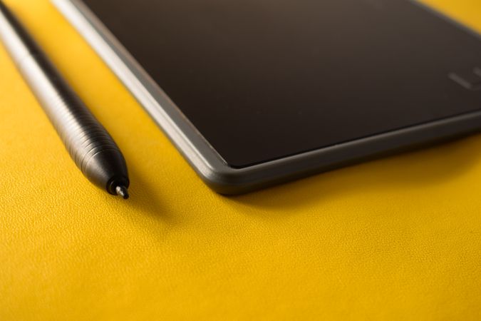 Close up of digital tablet and stylus on yellow table with space for text