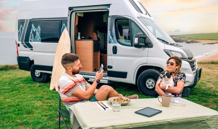 Male taking photo of female sitting at table outside with cute dog