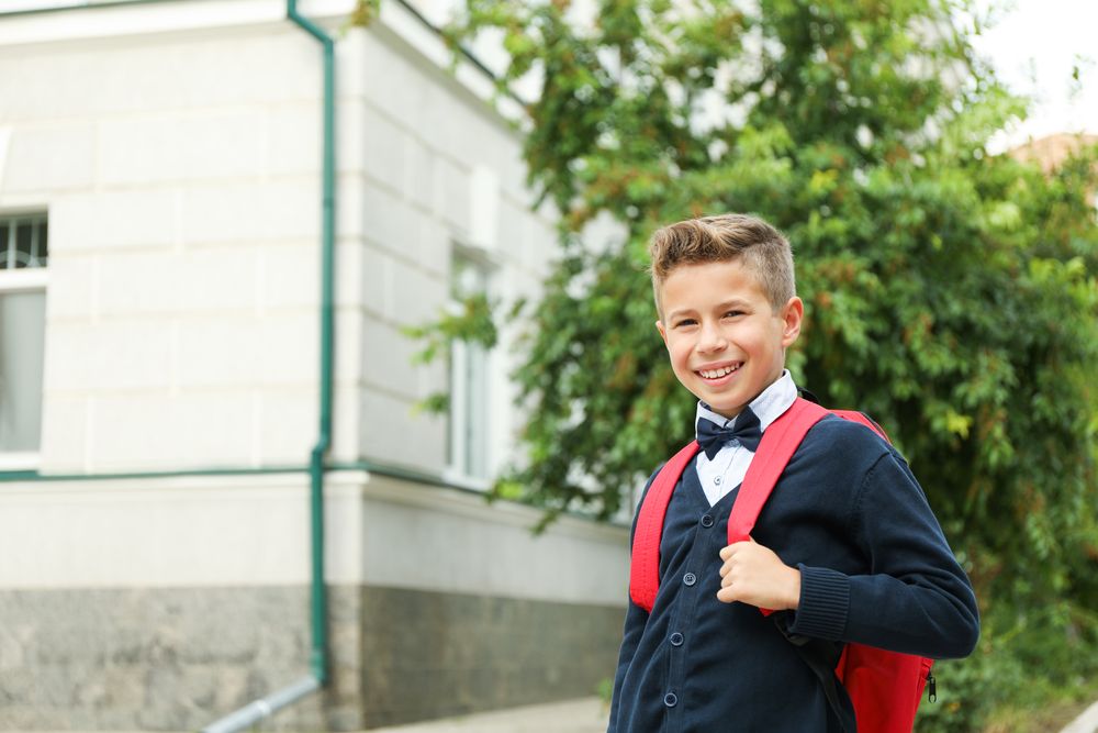 Boy with backpack against school building, space for text