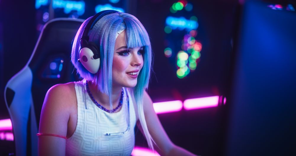 Smiling Cosplayer Talking to Her Online Friends on Desktop Computer While Sitting in Futuristic Cyberpunk Neon Home.