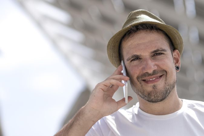 Happy male in hat speaking on phone outside