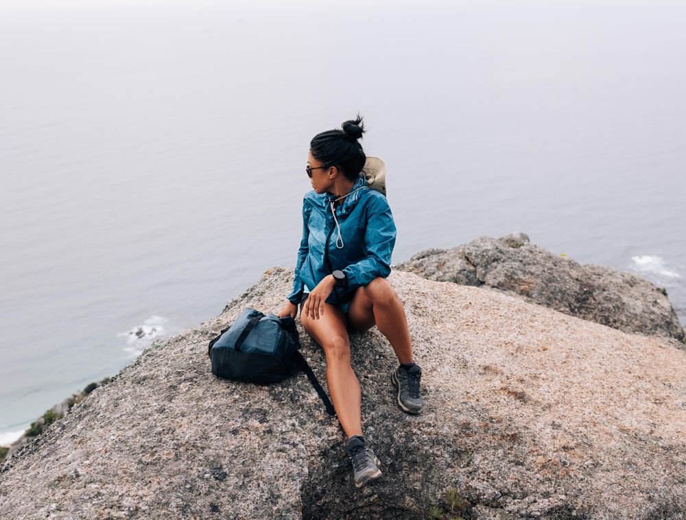 Female sitting on rock looking over view of ocean on overcast day