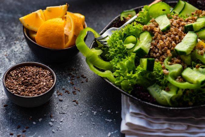 Green fresh salad with buckwheat on concrete background served with flax seed and lemon