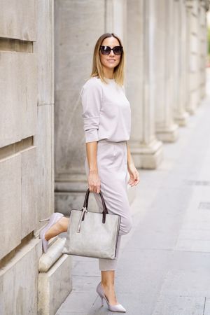 Chic woman in grey standing outside columns with bag