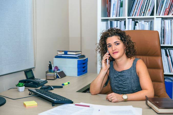 Businesswoman talking on phone in the office with bookcase