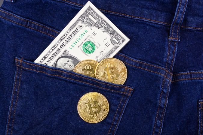 Bitcoins and dollar bill in denim pocket