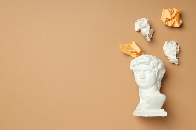 Marble bust with crumpled paper coming out of brain on brown background, copy space