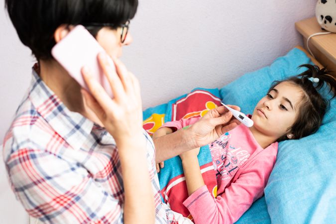 Mother on phone while taking daughter’s temperature