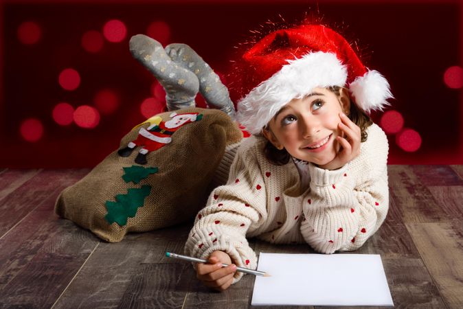 Cute girl thinking about writing a letter to Santa at Christmas time