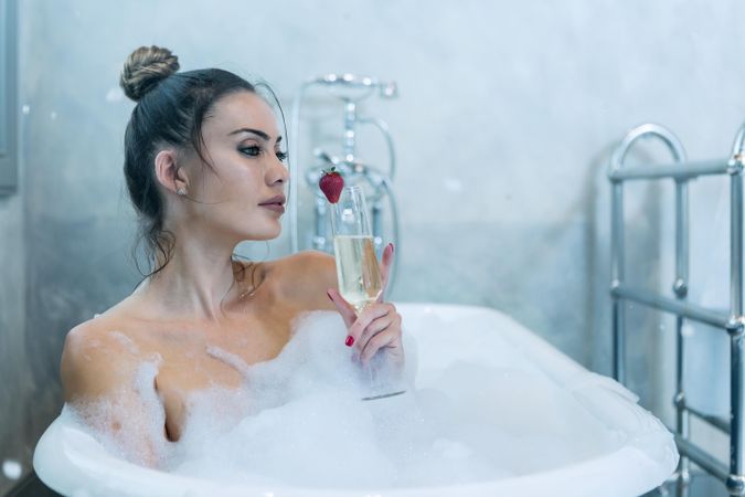 Dreamy woman drinking champagne in bathtub
