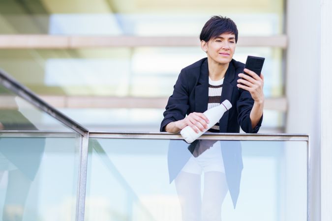 Woman taking break from work leaning outside of building checking phone