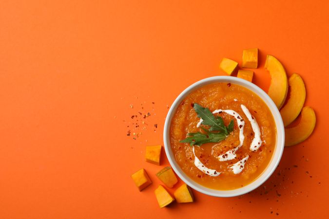 Top view of bowl of pumpkin soup on orange table with copy space