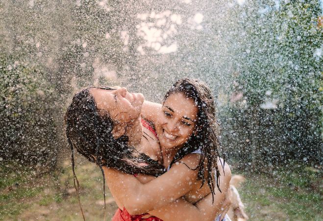 Friends in swimsuits hugging under water drops