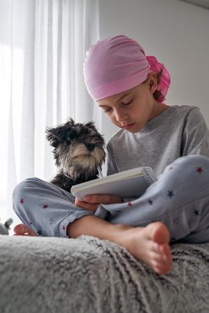 Serious kid in pink scarf writing in planner near dog