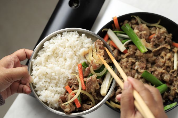 Hands putting together Korean rice and beef bowl