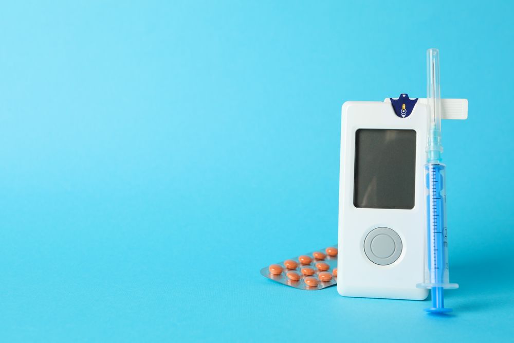 Blood glucose meter, syringe and pills on blue background