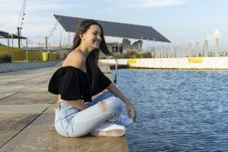 One young woman with long hair sitting with crossed legs on promenade while smiling and looking in the distance