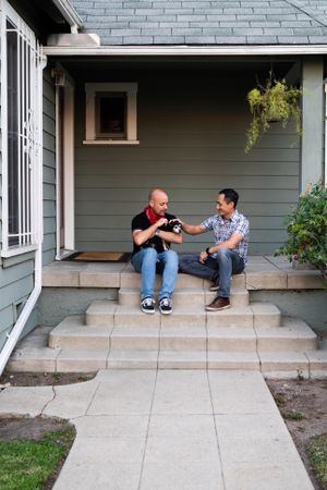 Two men sitting with their pet dog on front porch of house