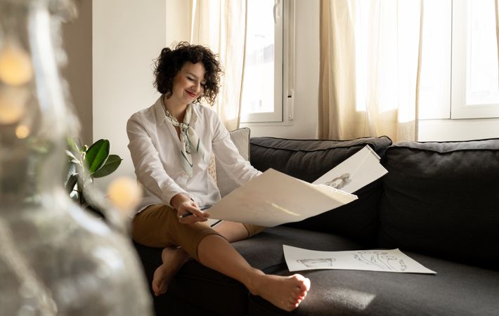 Woman drawing on papers on sofa in room