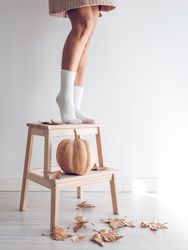 Crop woman on wooden ladder with pumpkin
