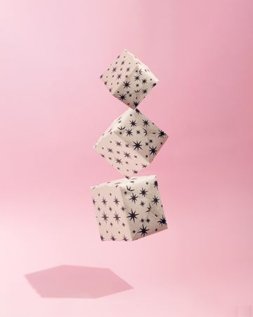 Three gift wrapped Christmas presents suspended on soft pink background with shadow
