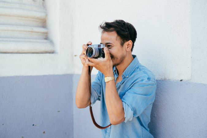 Man in blue shirt holding camera to his face smiling and taking photos