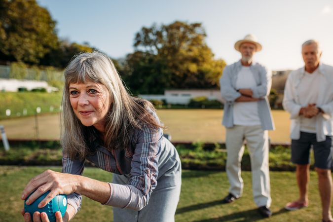 Close up of woman playing boules with her male friends standing in the background