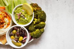 Tasty hummus and sauces decorated with bright cut vegetables on table