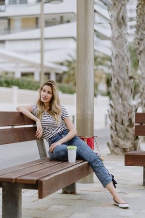 Happy woman with disposable cup of coffee sitting on street bench