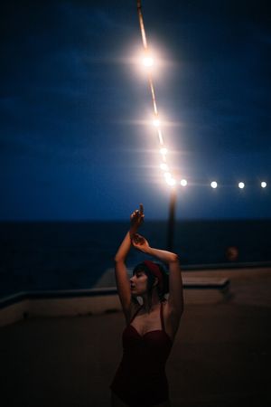 Mysterious woman in retro swimsuit dancing under streetlamp