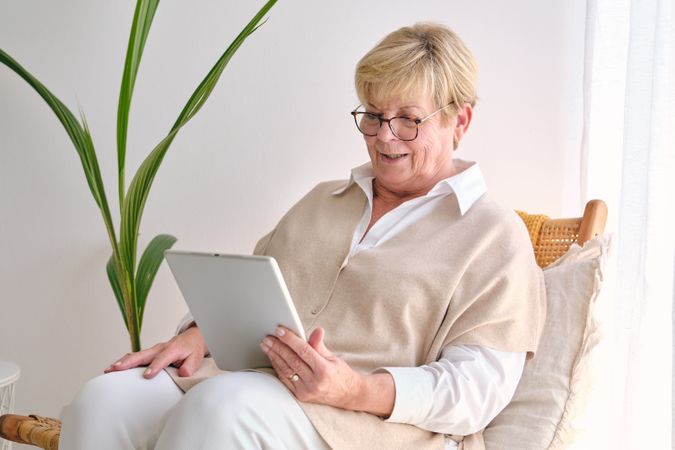 Smiling mature woman with tablet on wicker chair at home