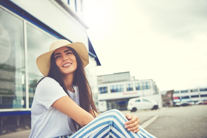 Woman with straw hat and striped trousers sitting on curb outside