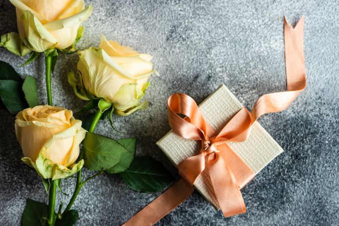 Top view of yellow flower on grey table with small present with copy space