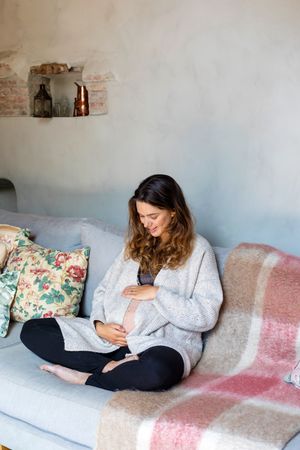 Pregnant woman happily holding her stomach on sofa
