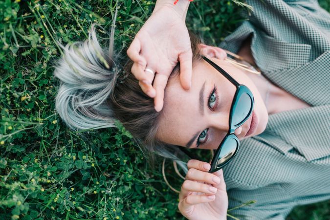 Woman in stylish suit and sunglasses lying in grass