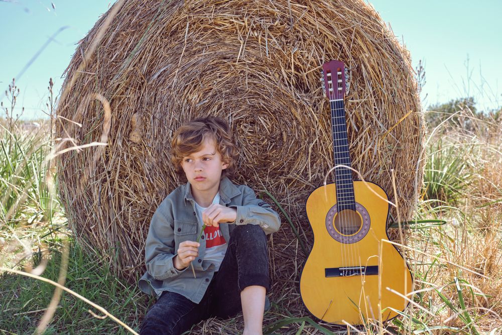 Upset kid sitting near guitar and leaning on hay bale