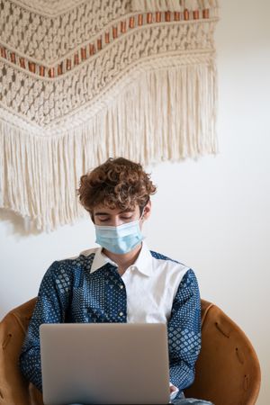 Nonbinary person wearing a face mask and sitting with a laptop
