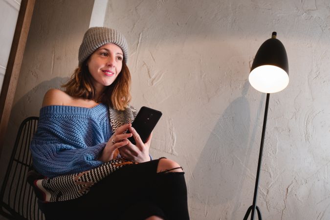 Woman in sweater and hat on the mobile phone and sitting near wall