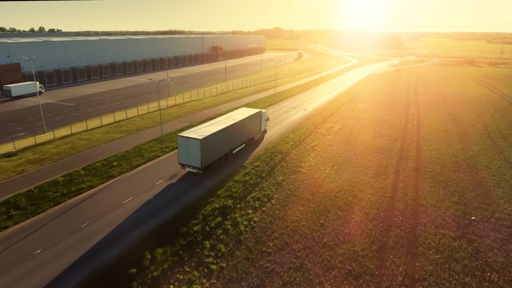 Aerial Shot of Semi Truck with Cargo Trailer Attached Moving Through Industrial Warehouse, Rural Area