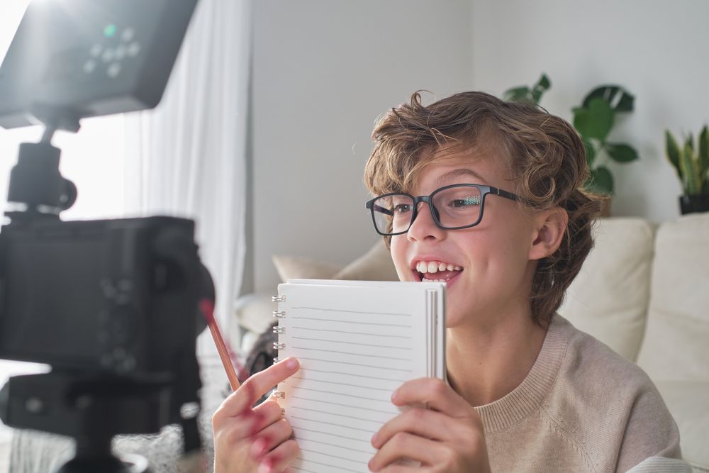 Smart positive boy in glasses recording video on camera at home