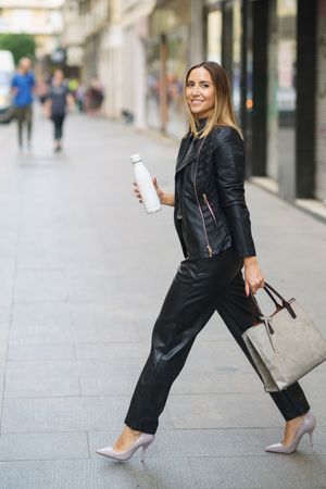 Stylish woman with bag and bottle walking on street