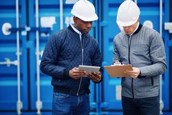 Two men in hardhats with tablet and notes
