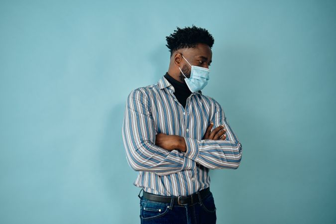 Portrait of a Black man in face mask blue striped shirt with his arms crossed looking away