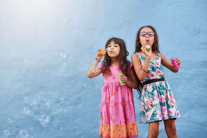 Portrait of adorable little girls blowing bubbles against a blue wall