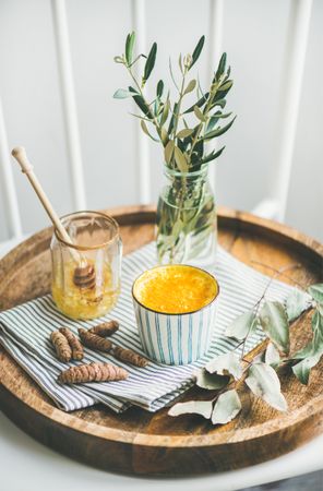 Warm turmeric latte in ceramic cup on wood tray with raw honey