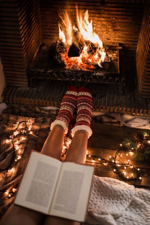 Unrecognizable woman sitting by fireplace and reading book