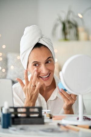 Smiling woman smearing facial cream under eyes while recording