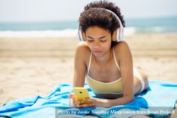 Female with curly hair on beach towel reading phone 5X9lk4